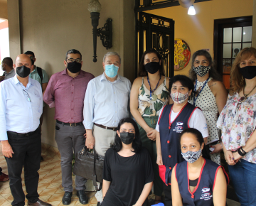 Grupo de pessoas posando para uma foto, todas usando máscaras, em frente a uma entrada de prédio